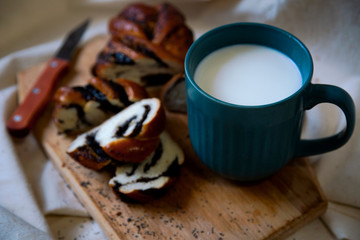 Sliced bun with poppy seed filling on a wooden Board and a mug of milk