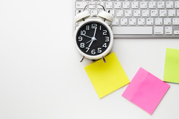 Office desk table with keyboard and alarm clock on white background, stickers yellow, purple and green color. Top view and copy space, flat lay