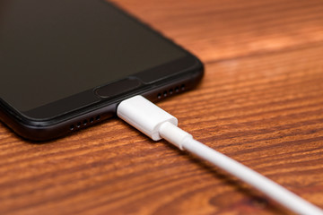 Close up smart phone charging with cable on wooden table. USB cable for smartphone on wood...