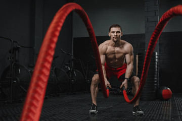 Muscular man doing battle ropes exercise at the crossfit gym