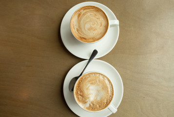 Two cups of cappuccino with latte art in white cups on wooden table. Morning coffee for couple in love. Top view. 