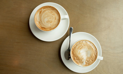 Two cups of cappuccino with latte art in white cups on wooden table. Morning coffee for couple in love. Top view. 