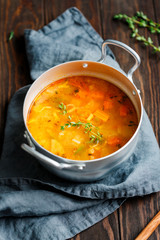 Spring vegetable soup with chicken stock in a pot on kitchen wooden table. Rustic style, close-up view.