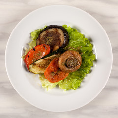Fried mushroom champignon, eggplant, tomato and green leaf lettuce on a white round plate.