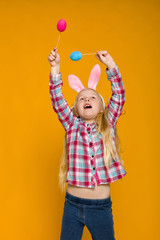 Portrait of cute little child girl with Easter bunny ears holding colorful eggs on yellow background. Happy easter
