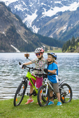 Children make Selfie by bike on the lake in a beautiful mountain landscape