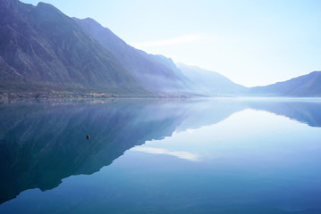 Morning in Boka Bay, Montenegro: high mountains and their reflection in calm sea water.