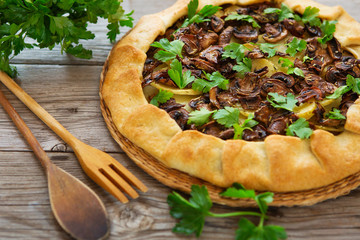 savory galette with potatoes, champignon and greenery on a wooden background, top view.