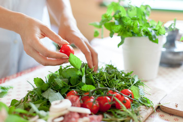 Woman is cooking in home kitchen. Female hands choose cherry tomatoes, vegetables for recipe....