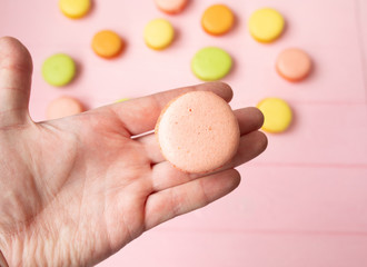 Hand holding Sweet and colourfull french macaroons or macaron on pink background