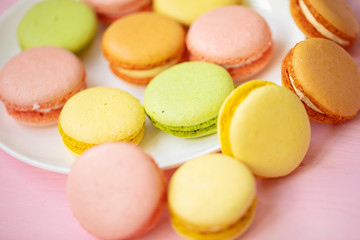 Colorful French or Italian macarons stack on white plate put on pink wood table with copy space for background. Dessert for served with afternoon tea or coffee break.