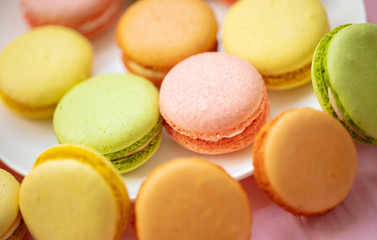 Colorful French or Italian macarons stack on white plate put on pink wood table with copy space for background. Dessert for served with afternoon tea or coffee break.