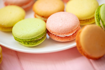 Obraz na płótnie Canvas Colorful French or Italian macarons stack on white plate put on pink wood table with copy space for background. Dessert for served with afternoon tea or coffee break.