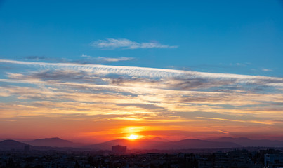 Sunset view Athens, Greece. Sun falling over mountains, blue sky with clouds background