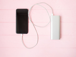 Phone charging with energy bank. Depth of field on Power bank. Pink wooden background.