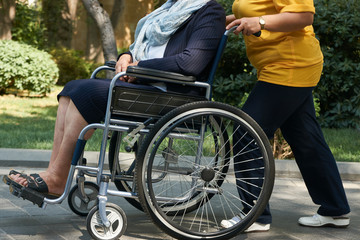 Obraz premium Disabled woman in a wheelchair relaxing in a park with a care assistant