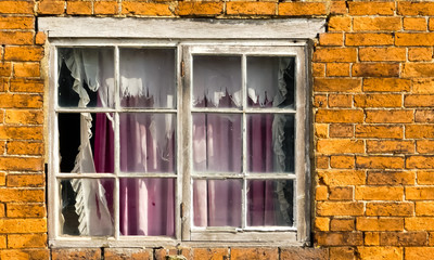 Detail of derelict cottage, by towpath on Grand Union Canal. Weathered wooden window, with broken glass pane, ripped net and faded dirty pink curtain. Old brickwork, Bright sunshine, Whilton, England