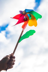 A colored Catherine wheel wind (pinwheel) with wooden stick. Shot from below with blue sky and clouds in the background, on a windy day. One hand holds the stick.