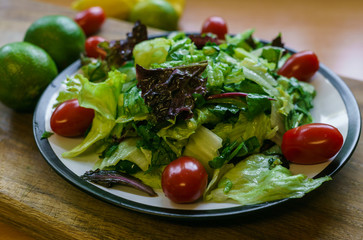 Fresh salad from different types of greens and cherry tomatoes, seasoned with olive oil and lime juice with lemon.