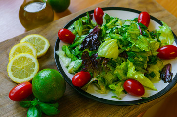 Fresh salad from different types of greens and cherry tomatoes, seasoned with olive oil and lime juice with lemon.