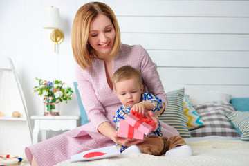 Happy family moment! Baby boy open gift box with beautiful mother.
