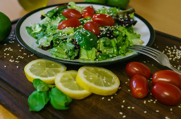 Fresh salad from different kinds of greens and a cherry tomato, dressed with olive oil and sprinkled with sesame seeds.