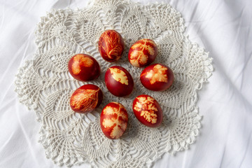 Easter eggs dyed with onion peels with a pattern of plants and leaves on a white lace doily, on the...