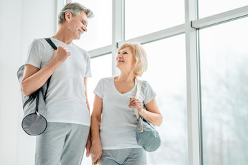 Easing into retirement with some yoga. Enjoying company with each other. Senior couple going on the sport training and carry bags with yoga mat. Health and sport lifestyle.