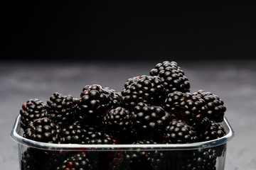 Blackberry in plastic container on empty black background
