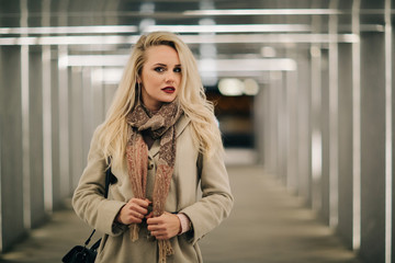 Blonde in coat at underpass.