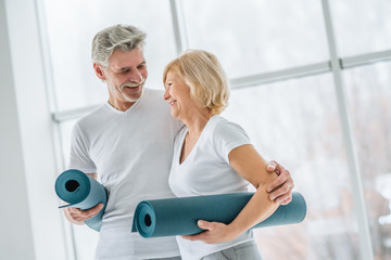 Health and sport concept. Senior couple with yoga mats in the gym.