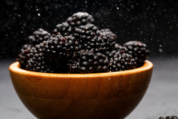 Photo of blackberry in wooden cup on empty black background.