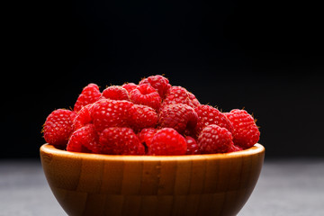Photo of raspberries in wooden cup on black background