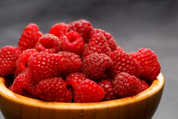 Photo of raspberries in wooden cup on black background