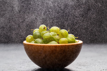 Photo of gooseberry berries in wooden cup and powder powdered sugar