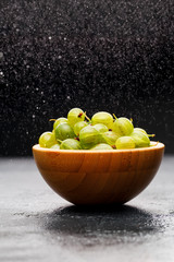 Photo of gooseberry berries in wooden cup and powder powdered sugar