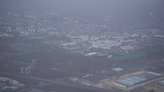 Aerial view of the outskirts of Paris with illuminated highway through the fog. Green forest areas, modern city buildings and industrial area.