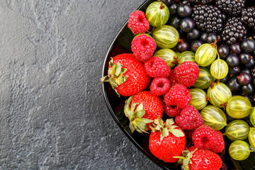 Photo on top of blackberries, strawberries, raspberries, gooseberries,black currant on black plate