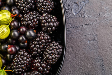 Photo on top of blackberries, black currant on black plate on black empty background