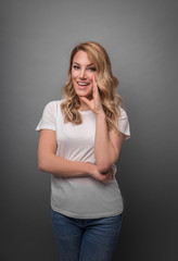Beautiful blonde speaks about something secretly posing on a gray background.
