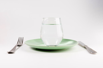 glass of water in a plate with knife and fork isolated on white background