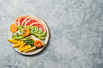 Assorted fruit on a plate, restaurant. Grapefruit, tangerine, kiwi, orange, banana, Apple. Gray background, top view, space for text