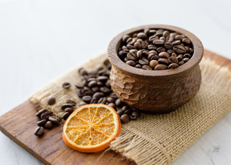 Closeup of coffee beans in wooden rustic bowl on bright background decorated with orange slice.