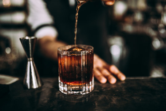 A close up shot of a bartender pouring whiskey. Classic old fashioned cocktail served with a cube of ice. Concept of bourbon whisky, spirits and alcohol.
