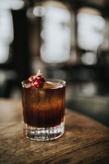 A close up shot of classic Old Fashioned cocktail served with a cube of ice and garnished with cranberries. Concept of bourbon whisky, spirits and alcohol.