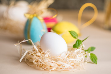 Ester chicken egg on straw against the background of decorative colored eggs made of wool