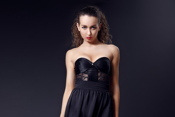 Fototapeta na wymiar Portrait of fashionable elegant girl in black evening dress on dark background. Evening look. Concept formal prom party