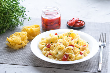 Italian traditional pasta tagliatelle with dried tomatoes and thyme on a light background.