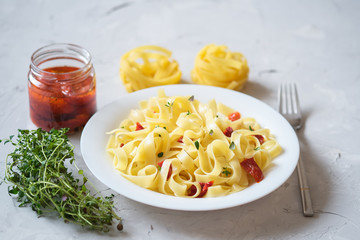 Italian traditional pasta tagliatelle with dried tomatoes and thyme on a light background.