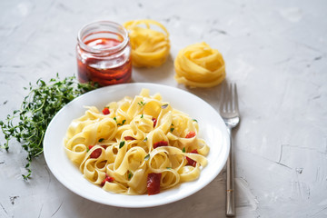 Italian traditional pasta tagliatelle with dried tomatoes and thyme on a light background.